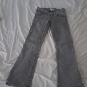 Grå bootcut jeans med fickdetaljer - Säljer ett par grå jeans med bootcut passform och snygga fickdetaljer med knappar bak. 