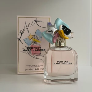 Perfect EdP 50ml från Marc Jacobs - Säljer en flaska Perfect Eau de Parfum från Marc Jacobs, 50 ml. Flaskan är transparent med ljusrosa parfym och har en unik kork dekorerad med färgglada detaljer som stjärna, banan och rosett. Kommer med originalkartong med konstnärlig design. Den är ändast använd 1 gång för ”lukt test”. Säljer pga inte min typ av doft💕