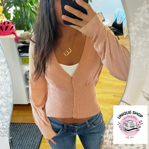 Ljusrosa glittrig kofta med knappar - Superfin ljusrosa kofta med glittriga detaljer och v-ringad hals. Modellen är croppad med långa ärmar och knappar framtill. Perfekt att styla med jeans eller kjol för en chill look. Materialet känns mjukt och stretchigt, passar dig som gillar comfy men snyggt.