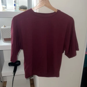 Vinröd t-shirt från 157, storlek M - En enkel och stilren vinröd t-shirt från 157 i storlek M. T-shirten har rund hals och korta ärmar, perfekt för dig som gillar basic plagg med lite färg. Materialet känns mjukt och skönt mot huden, troligtvis bomull. Passformen är normal och funkar till många olika stilar. Den går in i midjan 