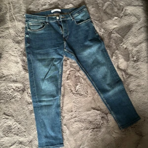 Blå jeans från Zara Denimwear - Snygga blå jeans från Zara Denimwear med klassisk femficksdesign och raka ben. Jeansen har en mörkblå tvätt med lätt slitning och kontrastsömmar. Storlek 38 vilket motsvara M
