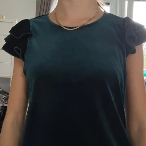 Mörkgrön sammetstopp Jacqueline de Yong - Supersnygg mörkgrön topp från Jacqueline de Yong i sammetsmaterial. Toppen har rund hals och coola volangdetaljer på axlarna som ger extra attityd. Perfekt för dig som vill sticka ut med en unik look.