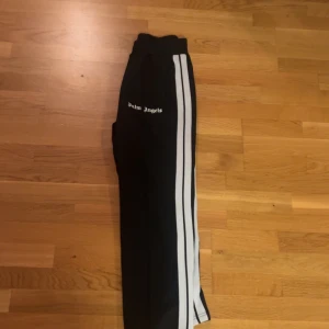 Palm Angels byxor - Svarta träningsbyxor från Palm Angels med två vita ränder längs sidorna. Säljes då jag ej använder:) storlek M