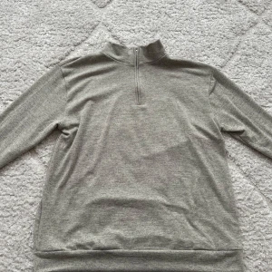 Grå halvzip tröja - Säljer en stilren grå tröja med halv dragkedja och hög krage. Perfekt för lager-på-lager och enkel att matcha med det mesta. Långärmad och i mjukt material som känns skönt mot huden. Kan vara en present till pappan(: