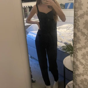 Svart byxdress med rosett - Säljer en svart byxdress med breda axelband och en snygg rosettdetalj framtill. Byxdressen har dragkedja i sidan och smock baktill för bättre passform. Man kan justera byxdressens längd med knappar💕byxdressen är använd nån enstaka gång😊