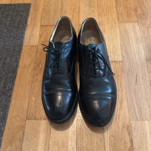 Svarta finskor läder från H.H. Brown - Klassiska svarta finskor i läder från H.H. Brown med rund tå och snörning. Skorna har en låg klack och stilren design som passar till många olika outfits. Perfekta för dig som gillar tidlös stil. Hål från hålslagare enligt bild.  