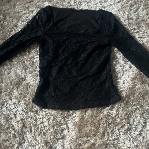 Svart spetsblus från BikBok - Säljer en svart långärmad blus från BikBok i spetsmaterial. Blusen har en fyrkantig ringning och är figurnära med fina spetsdetaljer över hela plagget. Perfekt för dig som gillar stilrena och eleganta toppar.