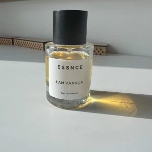 ESSNCE I Am Vanilla Eau de Parfum - En stilren parfymflaska med svart lock och transparent glas, fylld med en gyllengul vätska. Doften heter I Am Vanilla och är en Eau de Parfum från ESSNCE. Perfekt för dig som älskar varma, söta vaniljtoner.