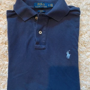Mörkblå pikétröja från Polo Ralph Lauren - Säljer en klassisk mörkblå pikétröja från Polo Ralph Lauren i storlek S! Tröjan har korta ärmar, krage och knäppning framtill samt den ikoniska broderade loggan på bröstet. Jag säljer den här pikén för ett otroligt pris, 299kr för en 8/10 skick polo piké (pris kan diskuteras)! Först till kvarn✅