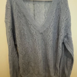 Ljusblå stickad tröja med v-ringning från Cider - Superfin ljusblå stickad tröja från Cider med djup v-ringning och ett snyggt hålmönster. Tröjan har långa ärmar och är perfekt för lager på lager stil. Passar både till jeans och kjol.