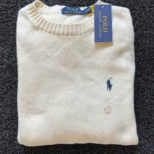 Vit stickad tröja från Polo Ralph Lauren - Säljer en klassisk vit stickad tröja från Polo Ralph Lauren med rund halsringning och broderad blå logga på bröstet. Tröjan är endast testad och den har prislappen kvar.