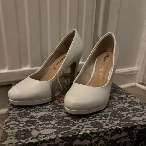Vita pumps från Tamaris - Säljer ett par klassiska vita pumps från Tamaris med rund tå och klack. Skorna har en stilren design och är tillverkade i syntetmaterial. Perfekta för dig som vill ha en enkel och elegant sko.