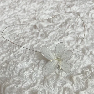 Halsband - Ett elegant handgjort halsband med en tunn metalltråd och en vit tygblomma med pärldetaljer i mitten. Perfekt för att ge en romantisk och drömmig känsla till din outfit.