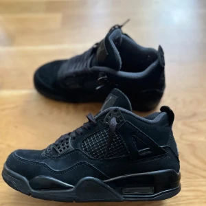 Svarta black cats st40 - Säljer ett par helsvarta Nike Air Jordans 4 sneakers med klassisk siluett och detaljer i mocka och syntet. Skorna har snörning, rund tå och platt sula. Perfekta för dig som gillar stilrena och sportiga sneakers.