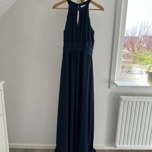 Mörkblå balklänning från VILA - Superfin balklänning från VILA i storlek 36. Den har hög halsringning och spetsdetalj i midjan. Använd en gång. Nypris 699.