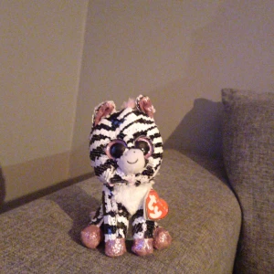 Zebramjukisdjur från Ty Beanie Boos - Säljer ett gulligt zebramjukisdjur från Ty Beanie Boos med stora glittriga ögon och rosa-glittriga tassar, öron och nos. och har svartvita ränder samt ett hjärtformat märke i örat. 