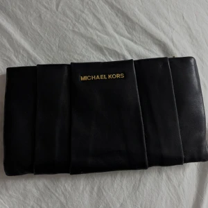 Svart kuvertväska från Michael Kors - Säljer en svart kuvertväska från Michael Kors storlek 26x14x2. Väskan är tillverkad i skinn och har flera fack inuti. Perfekt till en utekvällen.