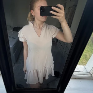 Ljusbeige/rosa klänning med volanger - Supersöt ljus beige/rosa klänning med volanger vid ärmar och nertill. V-ringad framtill och väldigt luftig. Klänningen  är till vardags men jag köpte den för att kunna spela tennis i den som jag spelade 1 gång och har inte gjort mer därmed säljer jag den🎾 💖 lite genomskinlig med svart annars aldrig!