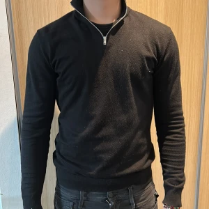 Lindbergh Svart half sip - Säljer en svart långärmad tröja med halv dragkedja i halsen. Tröjan har en smal passform och ribbade muddar vid ärmslut och midja. Perfekt för en stilren och enkel look.