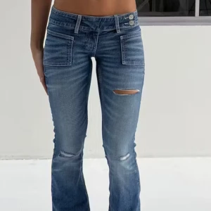 Blå bootcut jeans med slitningar - Snygga blå bootcut jeans med låg midja och slitningar på låret och knäna. Jeansen har framfickor med lock och klassisk knappgylf. 