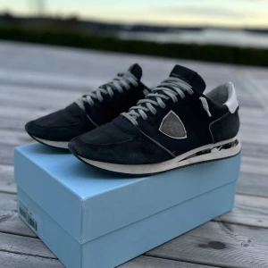  Philippe Model trainer - Säljer ett par svarta Philippe Model sneakers med vita detaljer och grå snörning. Skorna har en rund tå, platt sula och är tillverkade i mocka och skinn. Perfekta för dig som gillar stilrena och sportiga skor. Riktigt snygga och sköna skor. De har lite defekter som lite smuts men går säkert att tvätta sedan en liten spricka inne i skon i sulan men inget jag tänker på. Även lim som lostnat lite i sulan under men går att fixa