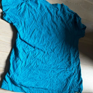 Turkos t-shirt från Adidas med blommigt tryck för barn  - Säljer en turkos t-shirt från Adidas med det klassiska logotyp-trycket i blommigt mönster framtill. T-shirten har rund hals och korta ärmar. Perfekt för dig som gillar sportig och färgglad stil! Denna T-shirten är för barn mellan 9-10 år