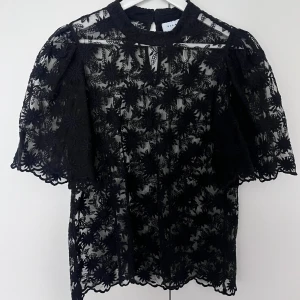Svart spetsblus med puffärm - Säljer en svart blus i spets med blommigt mönster och puffärmar. Blusen har hög hals och fina detaljer som ger en elegant look. Perfekt för både vardag och till finare tillställningar!!💗