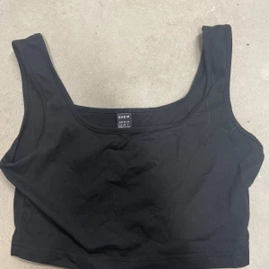 Svart croppad linnetopp från SHEIN - En enkel och stilren svart croppad linnetopp från SHEIN. Toppen har breda axelband och rundad halsringning, perfekt att matcha med jeans eller kjol. Mjuk och bekväm bomullskänsla.