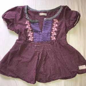 Rutig blus med broderi från Odd Molly - Superfin rutig blus i vinrött/lila och vitt från Odd Molly. Blusen har lila panel och rosa broderade blommor framtill. (bandet på sista bilden är lite slitet men fungerar fortfarande)