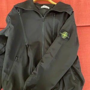Svart vindjacka från Stone Island - Säljer en svart vindjacka från Stone Island med klassisk logotyp på ärmen. Jackan är perfekt för dig för en stilren look