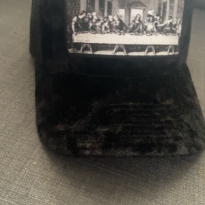 Keps - Passar alla, svart keps, glömt vad den heter, skick 9,9/10 använt 2 gånger tycker inte om den längre, bilden är jesus sista måltid, de är bara o skriva om ni har några frågor