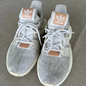 Sneakers Adidas - Sneakers från adidas. Grå/vit med puderrosa detaljer. Rejäl sula. Fint skick!