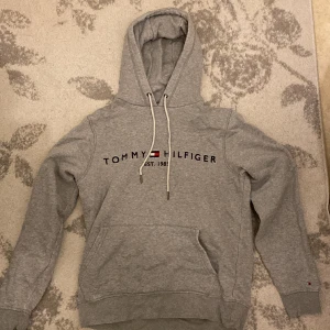 Grå hoddie - En skön Hoddie från Tommy hilfiger. Bra kvalite förutom lite hål vi handleden som ni kan se på bilden. Annars är tröjan bra.