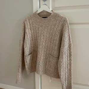 Beige stickad tröja  - Super söt tröja. Kabelstickad. Två ”fickor” som detalj fram. Använt fåtal gånger 