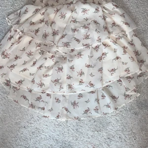 Blommig kjol - Vit, blommig sommarkjol. Slutar ovanför knät eller mitt på låret beroende på om man vill ha high-, mid- eller lowwaist. 100% polyester. 