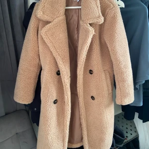 Teddy kappa - Så mysig Teddy kappa från NA-KD. Använd ca 5 gånger och är i väldigt fint skick. Storlek 32 men passar mig som har storlek S. Varm och perfekt till hösten eller våren