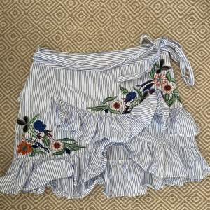 Gullig kjol med blommiga broderier. Sjukt fin och i bra skick. Har en dragkedja på vänster sida och ett band i midjan. 
