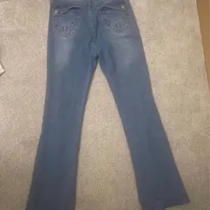 Ett par blåa jeans med dekorerade fickor. Storlek xs. Som du ser p bilden så har en del gått av men d går att sy ihop den igen. 