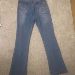 Ett par blåa jeans med dekorerade fickor. Storlek xs. Som du ser p bilden så har en del gått av men d går att sy ihop den igen. 