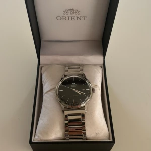 Orient herr klocka - Automatisk Orient klocka med bytt band ifrån läder till stål.  Extra länkar följes med.  Det är en mycket fin klocka i bra skick. Inga repor eller skador.    Orginalbox. 