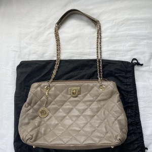 DKNY väska - 35cm x 24cm, grå/brunt tonad, inga synliga skador, bra skick, mycket fickor och utrymme innuti, finns en ficka i mitten av väskan med drag kedja som är perfekt för att ha sitt smink i och ha ordning i väskan.