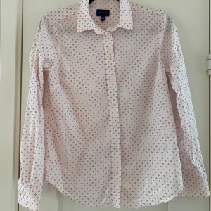 Vit skjorta med små röda hjärtan från Gant i strl 36 - Vit skjorta med små röda hjärtan från Gant i strl 36.  Sparsamt använd och i fint begagnat skick.  Mått Över bröstet: ca 45 cm Längd från axeln och ner: ca 67 cm  97% bomull och 3% elastan