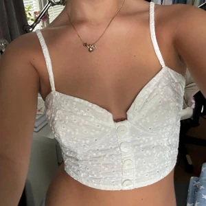 Vit korsettliknande topp med broderi och knappar från Zara - Säljer denna jättesöta vita korsettliknande topp med broderi och påsydda knappar från Zara, då den tyvärr inte kommer till användning. Använd en gång, därmed mycket bra skick. Smock i ryggen och lite stretch, passar XXS-liten S. 