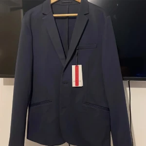 Mörkblå kavaj från Lindbergh - En elegant mörkblå kavaj från Lindbergh med en smal passform. Kavajen har två framfickor och en bröstficka. Den är tillverkad av högkvalitativa material med bra stretch för extra komfort och rörelsefrihet.