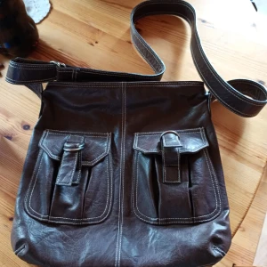 Brun skinnväska med axelrem. - Fin handväska skinn brun med två utanpå liggande fack och bra utrymme inne i väskan. Fint skick.