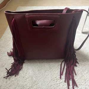 Vinröd väska - Säljer denna vinröda maje liknande väskan med fransar! några mindre defekter (syns på bild 3) samt en detalj jag klippte bort på ena sidan av väskan. Säljer för 350 ❤️‍🔥❤️‍🔥
