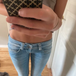 Ljusblå jeans med slitna detaljer - Säljer ett par ljusblå jeans i storlek S. De är lågmidjade och är boutcut. Jeansen är uppsprättade vid bensluten och en knappgylf med 2 knappar.💕