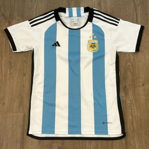 Vit och blå fotbollströja från Adidas - Säljer en argentisk landskapströja. Perfekt för fotbollsfans! Tröjan är i nyskick och redo att användas.