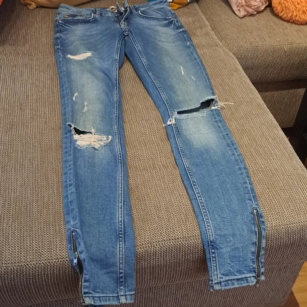 Säljer ett par blå jeans med slitningar och dragkedjor vid bensluten. Jeansen har en tight passform och är i en klassisk blå färg. Perfekta för en avslappnad och trendig look! knappt använd. passar Xs oxh S. Jeans & Byxor.