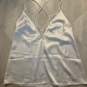 Vit linne med spets  - Ett snyggt vit linne i satinmaterial med spetskant. Låg rygg med korsande snören. Storlek 36 från Nelly. Aldrig använd. Använd gärna köpa nu <3 